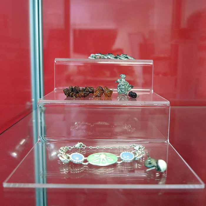 Frontansicht des transparenten dreistufigen Acrylpodests mit Schmuck auf den abgestuften Präsentationsflächen.
