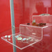 Seitliche Ansicht eines transparenten Acryl-Stufenpodests mit Schmuck auf rotem Präsentationshintergrund.